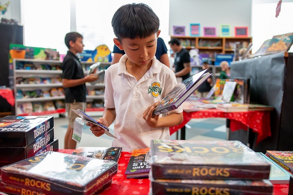 Fourth grade male student at the book fair looking down and finding books to purchase..