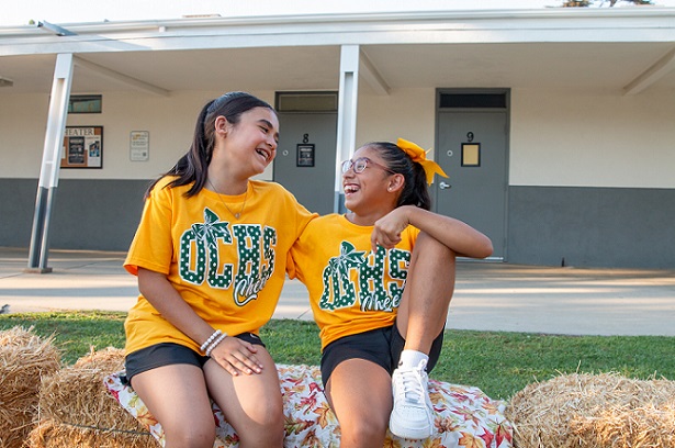 Two girls sitting on heystacks at the harvest festival laughing.