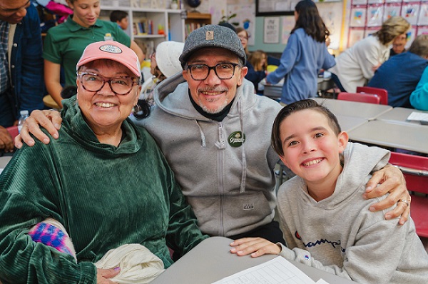 Elementary student sitting in a classroom with his grandparents smiling for a photo on Grandparents Day.