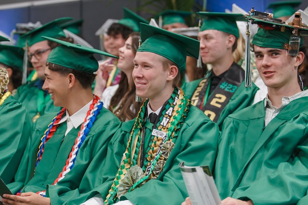 Three high school senior in their cap and gowns smiling at the crowd during the graduation ceremony.