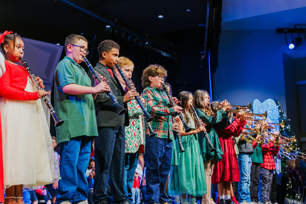 Three high school senior in their cap and gowns smiling at the crowd during the graduation ceremony.