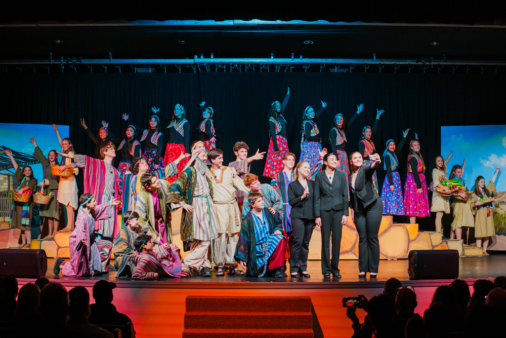 Three high school senior in their cap and gowns smiling at the crowd during the graduation ceremony.