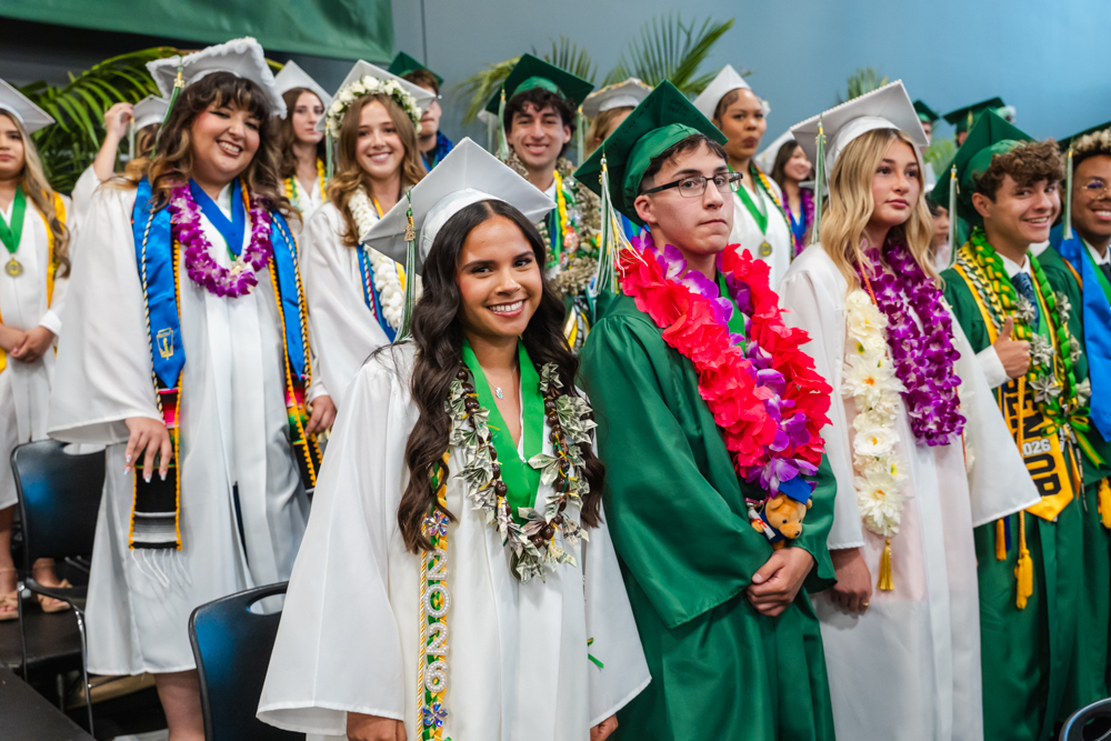Three high school senior in their cap and gowns smiling at the crowd during the graduation ceremony.